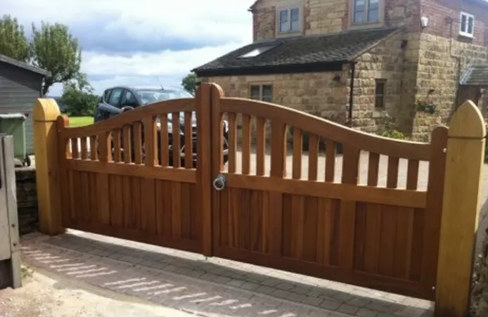 Pair of hardwood driveway gates with an arched top in front of a stone house